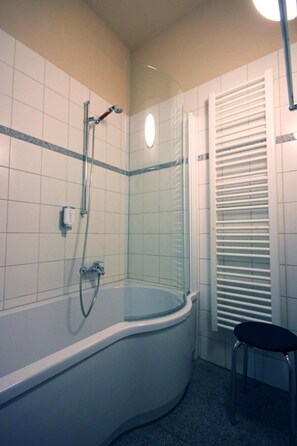 A bathroom with a glass-enclosed shower, a white bathtub, and a small stool. - Hotel Zittauer Hof (Zittau)