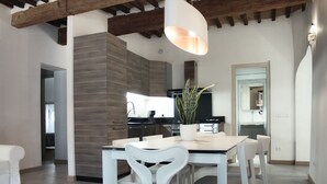 A modern kitchen with a built-in stove, a dining area with a white table and chairs, and a hanging light fixture. - Vicolo del Geppone (Lucca)