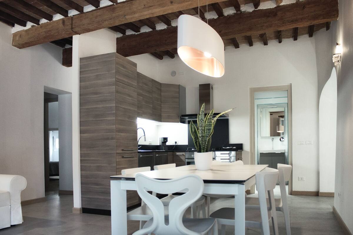 A modern kitchen with a built-in stove, a dining area with a white table and chairs, and a hanging light fixture.