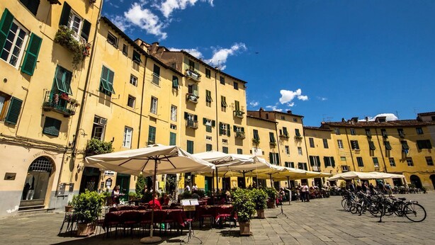 A square with outdoor seating, yellow buildings, and a clear blue sky. - Vicolo del Geppone (Lucca)