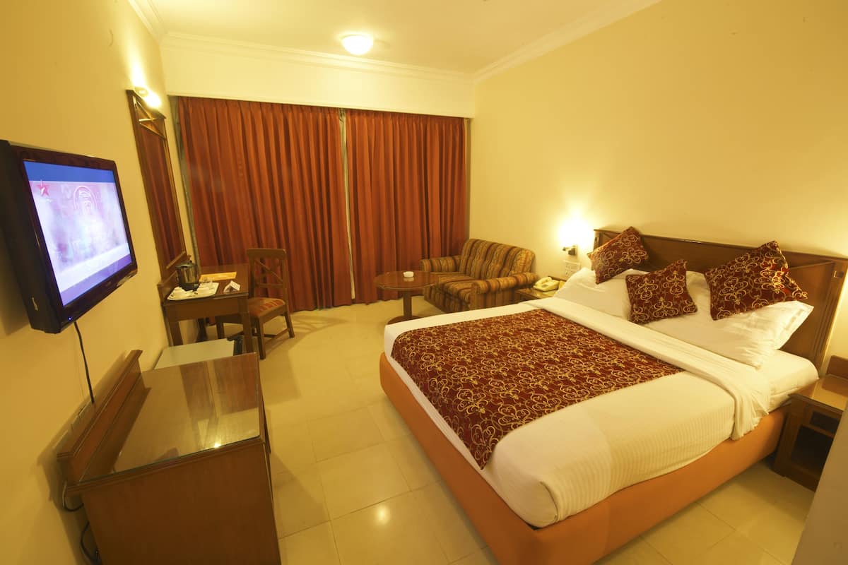Habitación de hotel con una cama grande, un escritorio, una silla, un televisor y una ventana con cortinas.