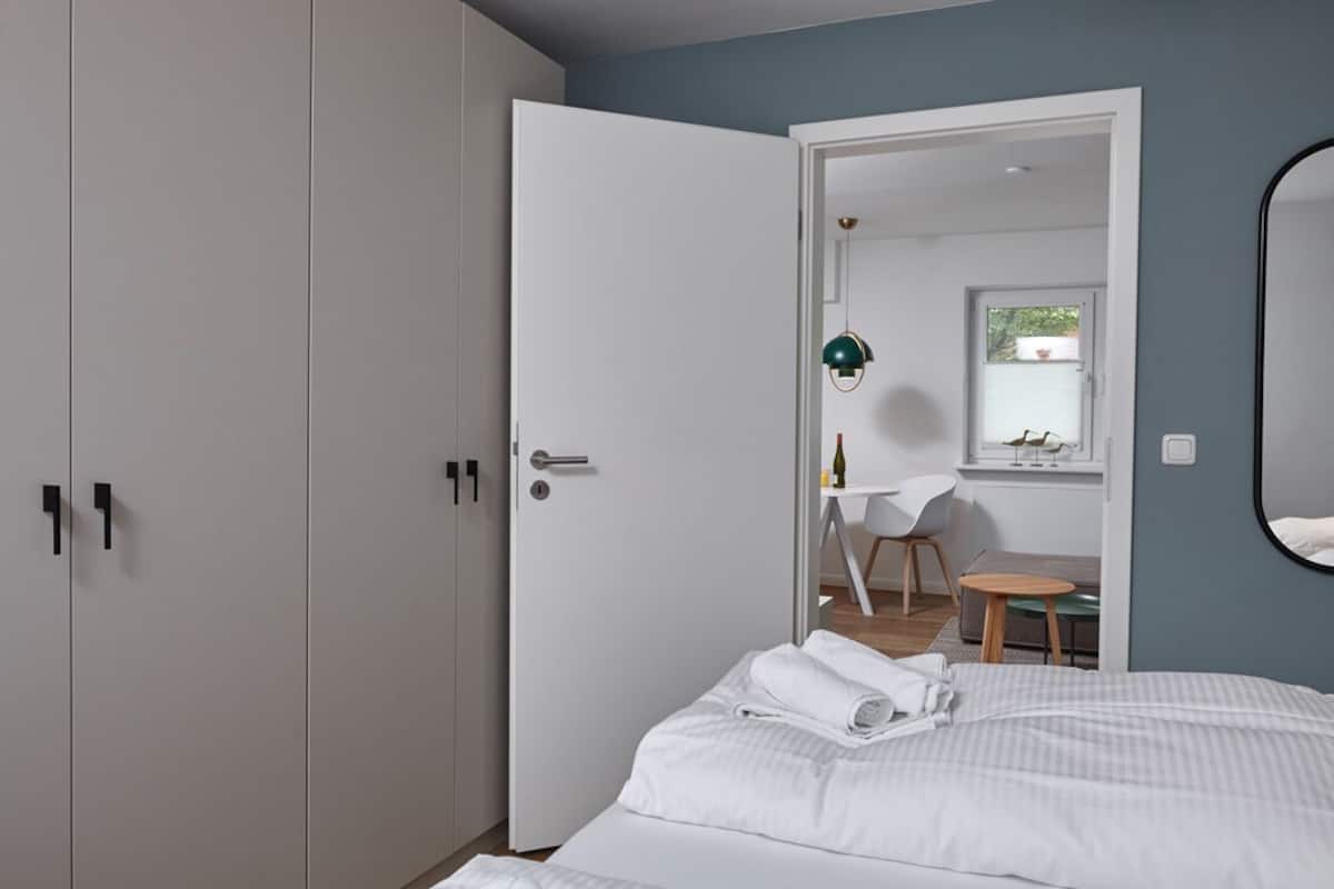 Ein Schlafzimmer mit einem Bett, einem weißen Wandschrank und einer Tür zu einem Essbereich mit Tisch und Stühlen.