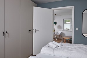 Un dormitorio con cama, armario blanco y puerta que da a un comedor con mesa y sillas.