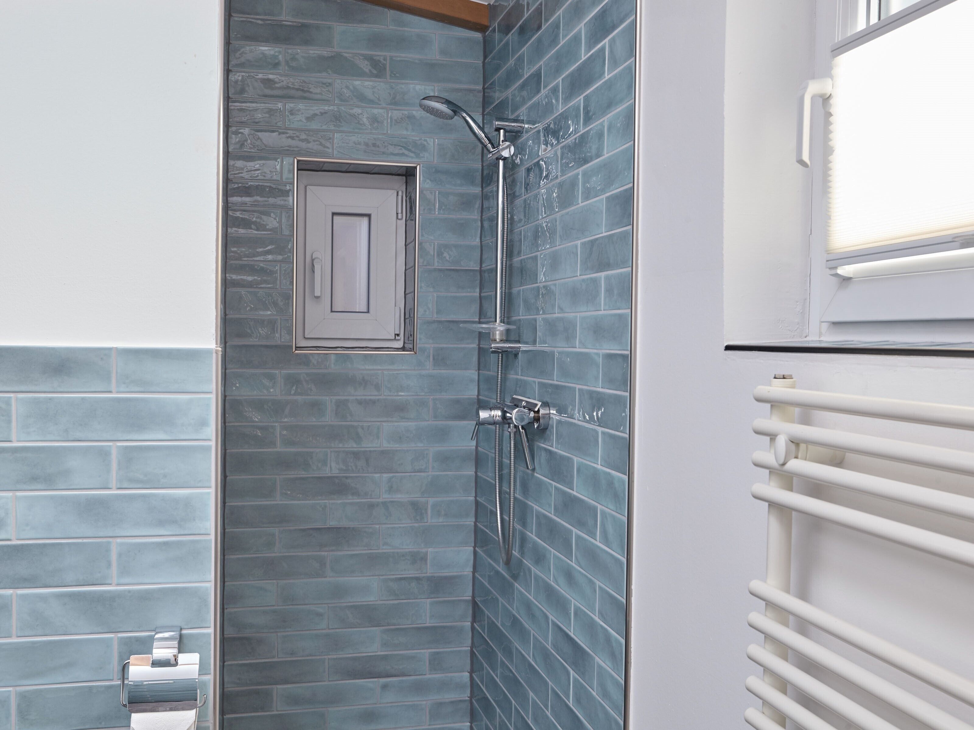 A bathroom with a shower, a towel rack, and a small window.