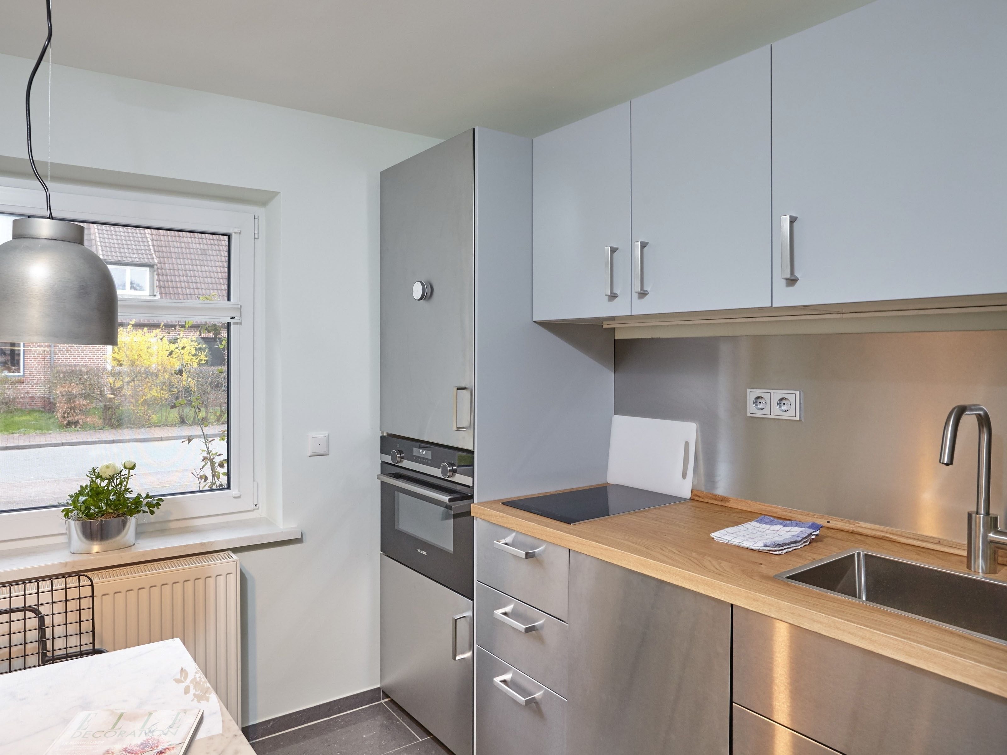 A modern kitchen with stainless steel appliances, a wooden countertop, and a window with a view of a garden.