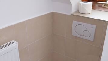 Une petite salle de bain moderne, équipée de toilettes, d’un radiateur et d’une fenêtre donnant sur un espace verdoyant.