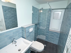 Baño con lavamanos, inodoro y zona de ducha, con paredes de azulejos azules y un ventanal.