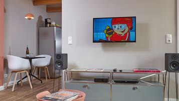 Ein modernes Wohnzimmer mit Flachbildfernseher, einer Kaffeemaschine, einem Bücherregal und einem Essbereich mit Stühlen.