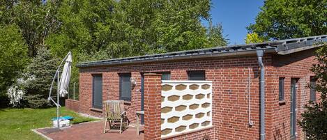 Een bakstenen gebouw met een terras, een witte hekken en een bank.