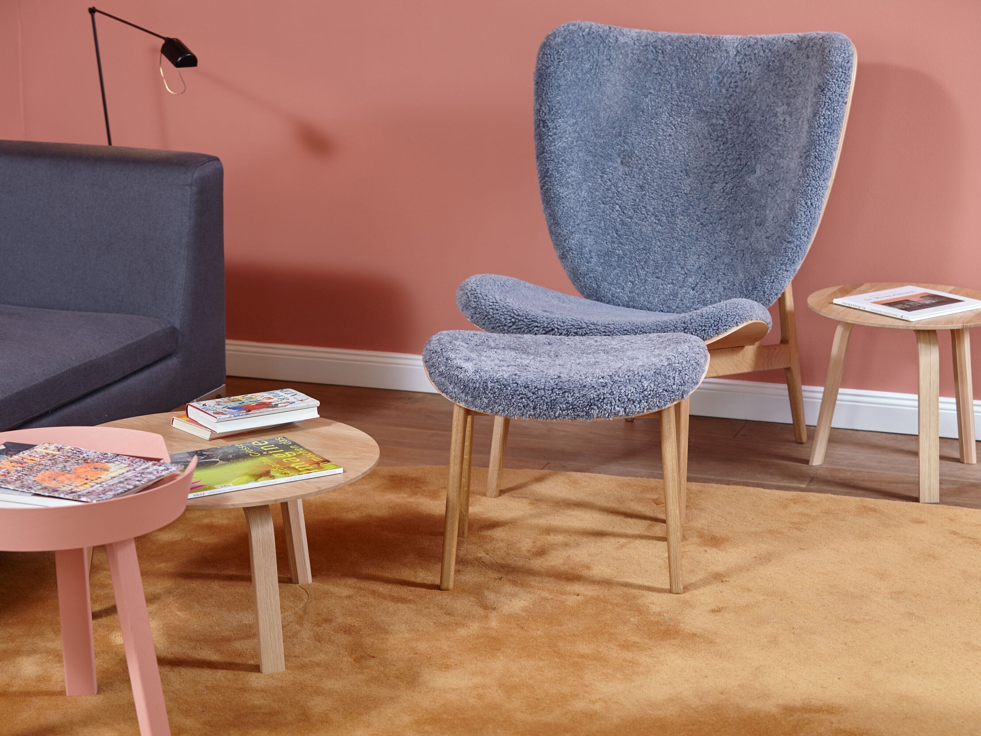 A modern living room with a grey sofa, a blue armchair, and a small round table with books.