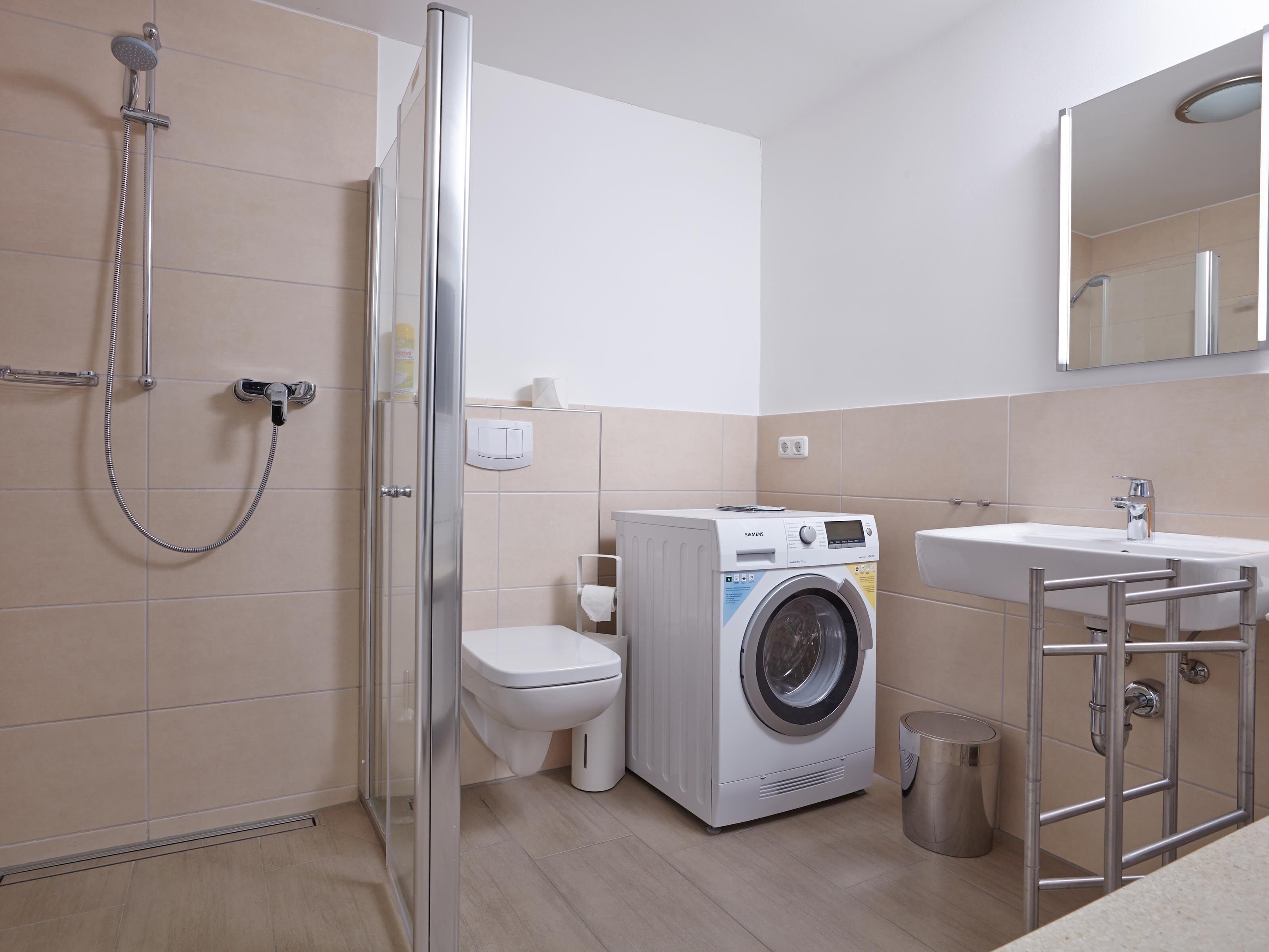A modern bathroom with a glass-enclosed shower, a washing machine, and a sink with a mirror above it.