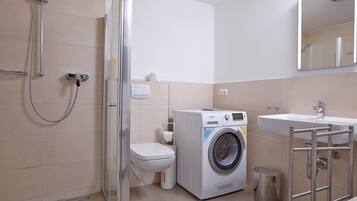 A modern bathroom with a glass-enclosed shower, a washing machine, and a sink with a mirror above it.