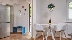 A modern kitchen with a stainless steel refrigerator, a blue stool, white chairs, and a table with a bottle of wine. - Ferienhäuser & Appartments Düneneck 6 (St. Peter-Ording)