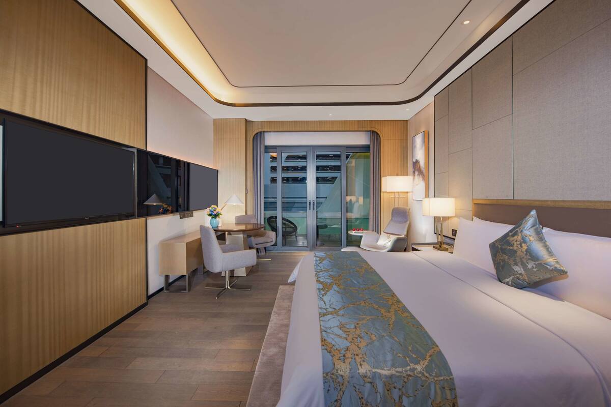 Une chambre d’hôtel moderne dotée d’un grand lit, d’une télévision à écran plat, d’un bureau avec une chaise et d’un coin salon avec deux fauteuils.