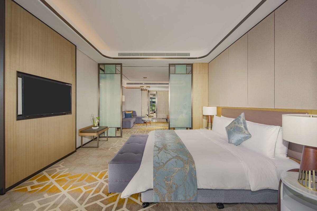 Une chambre d’hôtel moderne dotée d’un grand lit, d’un téléviseur à écran plat, d’un bureau avec une chaise et d’une petite table avec une lampe.