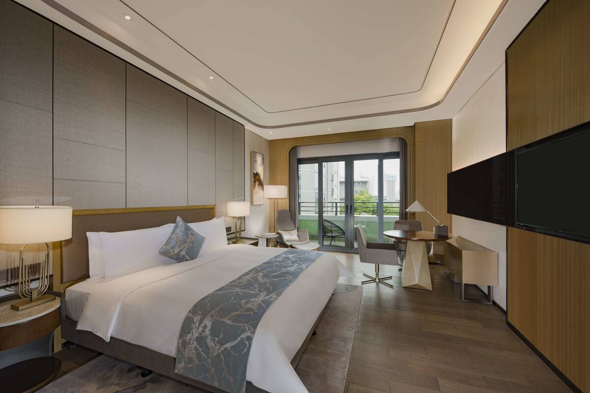 Une chambre d’hôtel moderne dotée d’un grand lit, d’une télévision à écran plat, d’un balcon avec vue et d’un bureau avec une chaise.