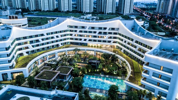Un hotel moderno de varios pisos con un patio central que cuenta con una piscina y zonas ajardinadas.