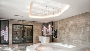 Un espacio moderno de spa con un jacuzzi grande y rectangular, un diseño de pared geométrico y una lámpara colgante.