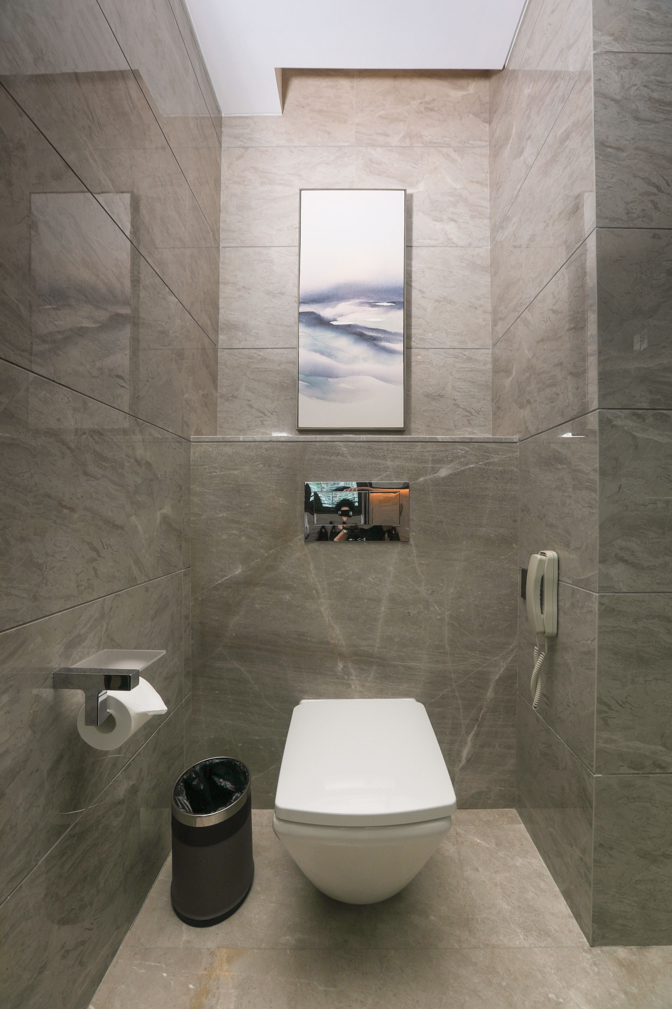A modern bathroom with a toilet, a trash can, a towel rack, and a framed picture on the wall.