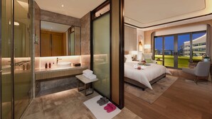 Una habitación de hotel moderna con una cama grande, un área de descanso, un baño con cabina de ducha de vidrio y un balcón con vistas a la ciudad.