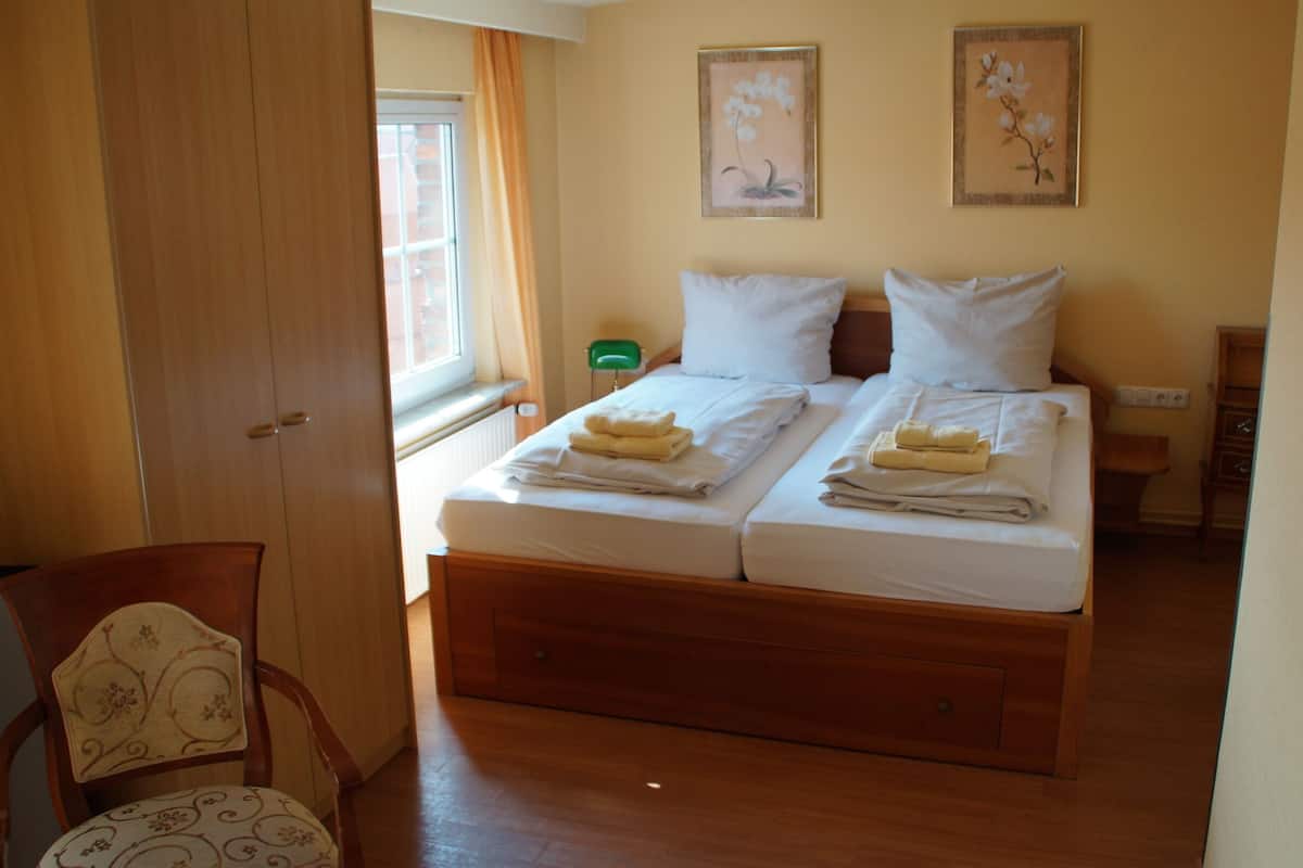 Une chambre avec deux lits, un plancher en bois, une chaise et un téléviseur.