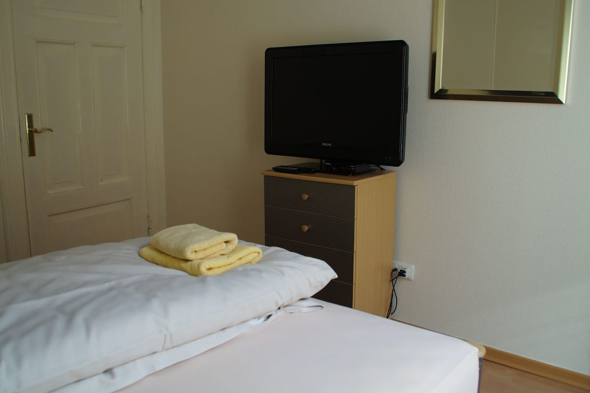 Une chambre d’hôtel avec un lit, un téléviseur posé sur une commode en bois et un miroir au mur.