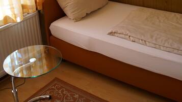 A small, single-bed room with a glass table, a radiator, and a painting on the wall.