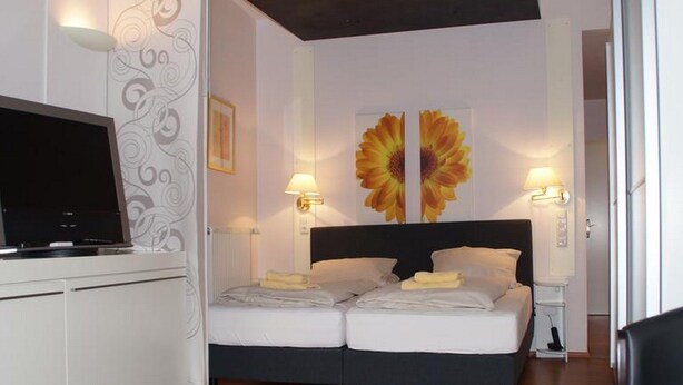 Een slaapkamer met een bed, bedlampen, een televisie op een kast en een groot bloemschilderij aan de muur.