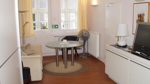 Een compacte kamer met een ronde glazen tafel, een bank, een televisie en een radiator.
