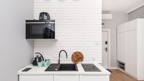Een moderne keuken met een witte bakstenen spatwand, een zwarte magnetron, een waterkoker en een houten bord aan de muur.