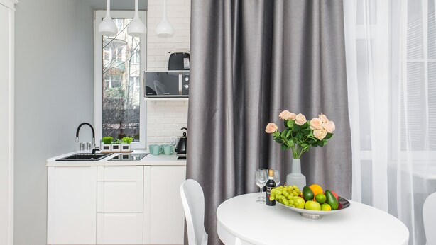 Een moderne keuken met witte kastjes, een zwarte magnetron en een raam met uitzicht op gebouwen.