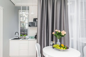 A modern kitchen with white cabinets, a black microwave, and a window with a view of buildings. - Noble Apartments (Kraków)