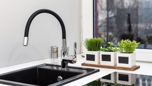 Een moderne keuken met een zwarte kraan, witte kasten en een raam met uitzicht op bomen.