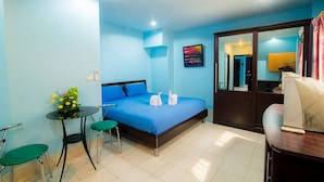 A hotel room with a bed, a small table with a vase of flowers, two green chairs, and a desk with a computer. - DE Apartment (Pattaya)