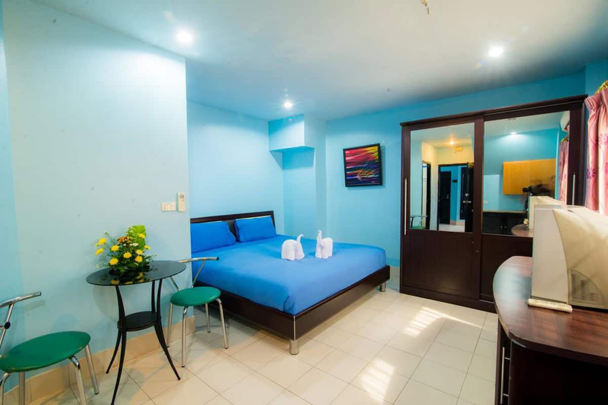 A hotel room with a bed, a small table with a vase of flowers, two green chairs, and a desk with a computer.