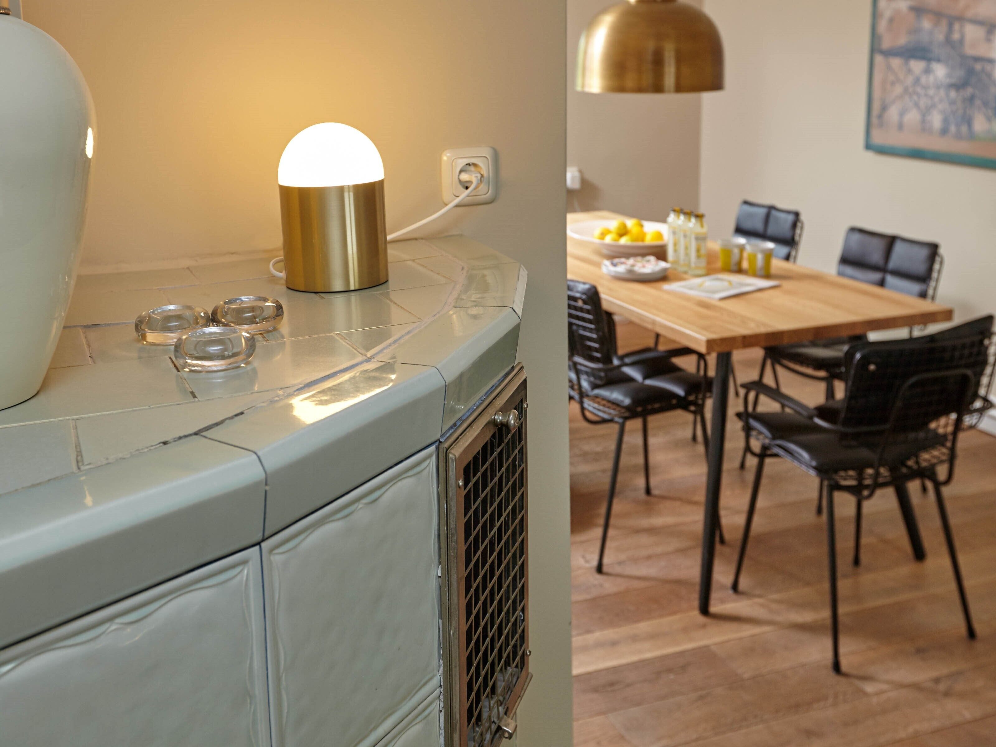 Una cocina con estufa antigua, una lámpara moderna y un comedor con mesa de madera y sillas negras.