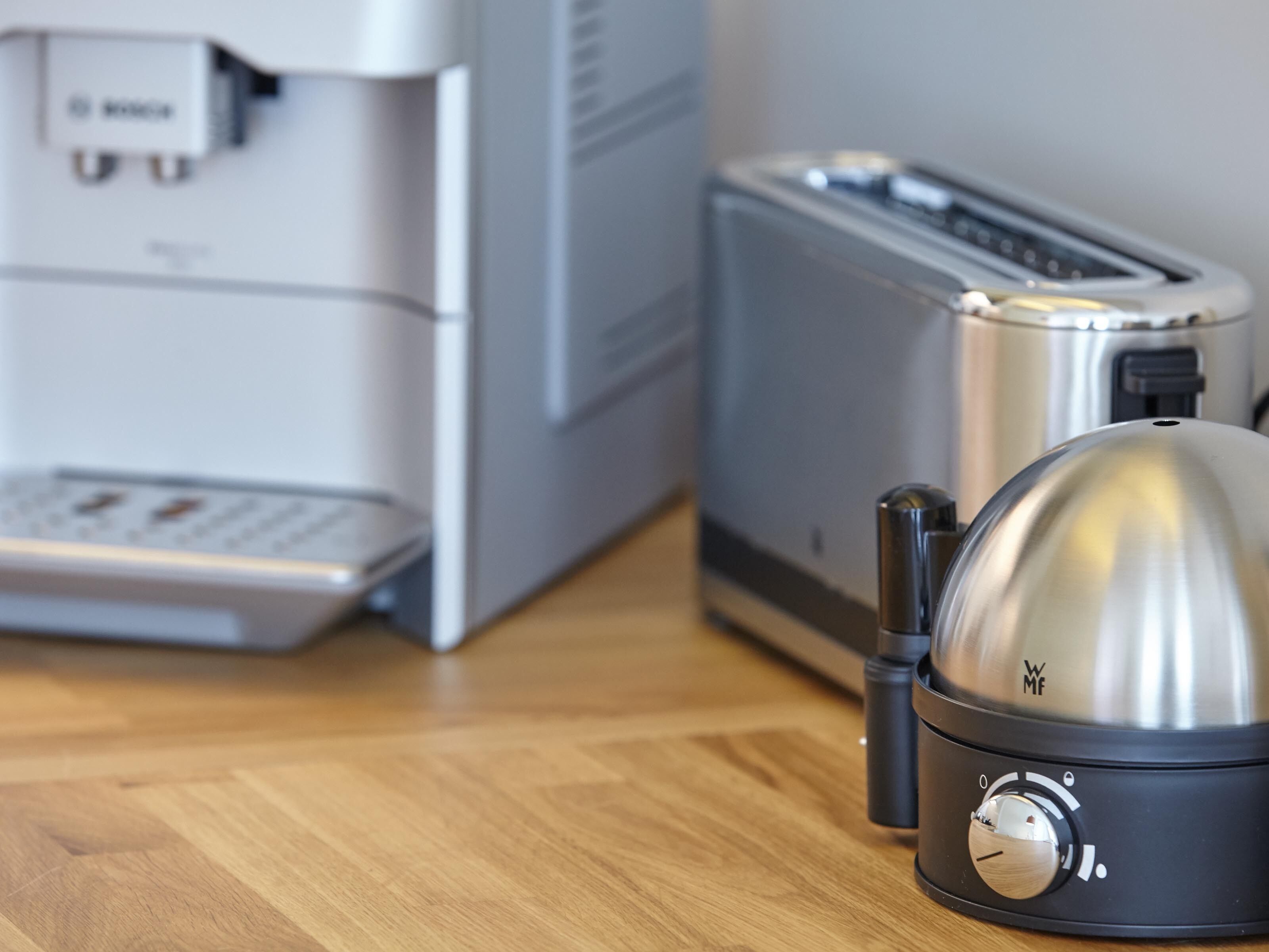 A kitchen with a coffee maker, toaster, and a kettle on a wooden floor.