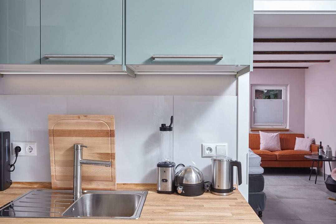 Een moderne keuken met een roestvrijstalen spoelbak, een houten snijplank, een blender, een waterkoker en een koffiezetapparaat.