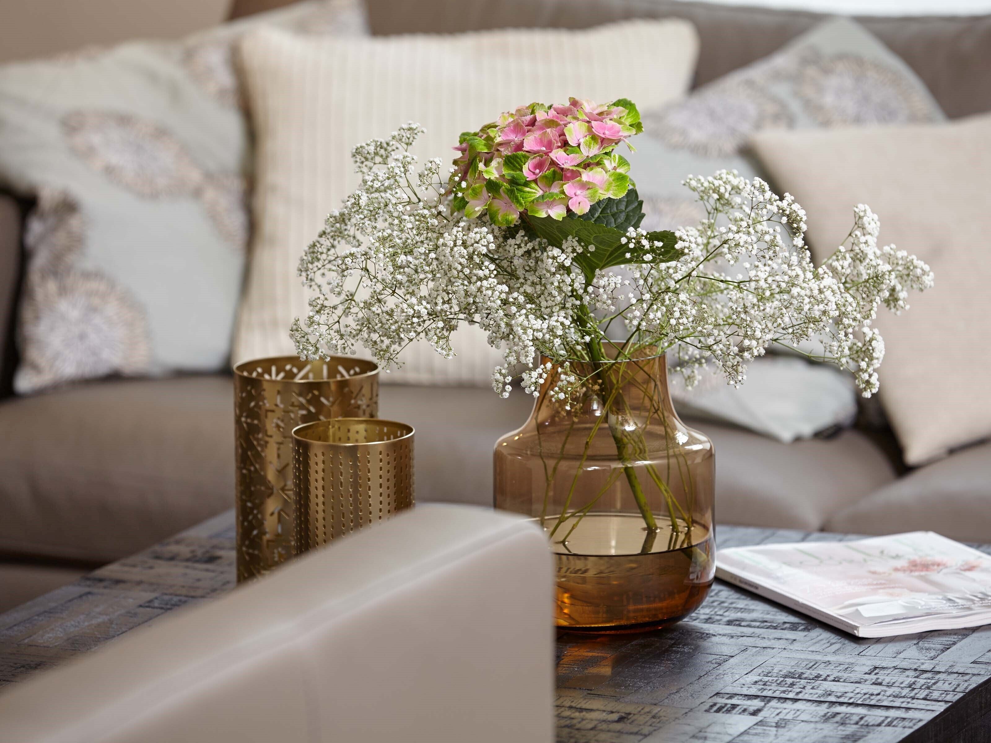 A living room with a sofa, a coffee table, and a vase with flowers.