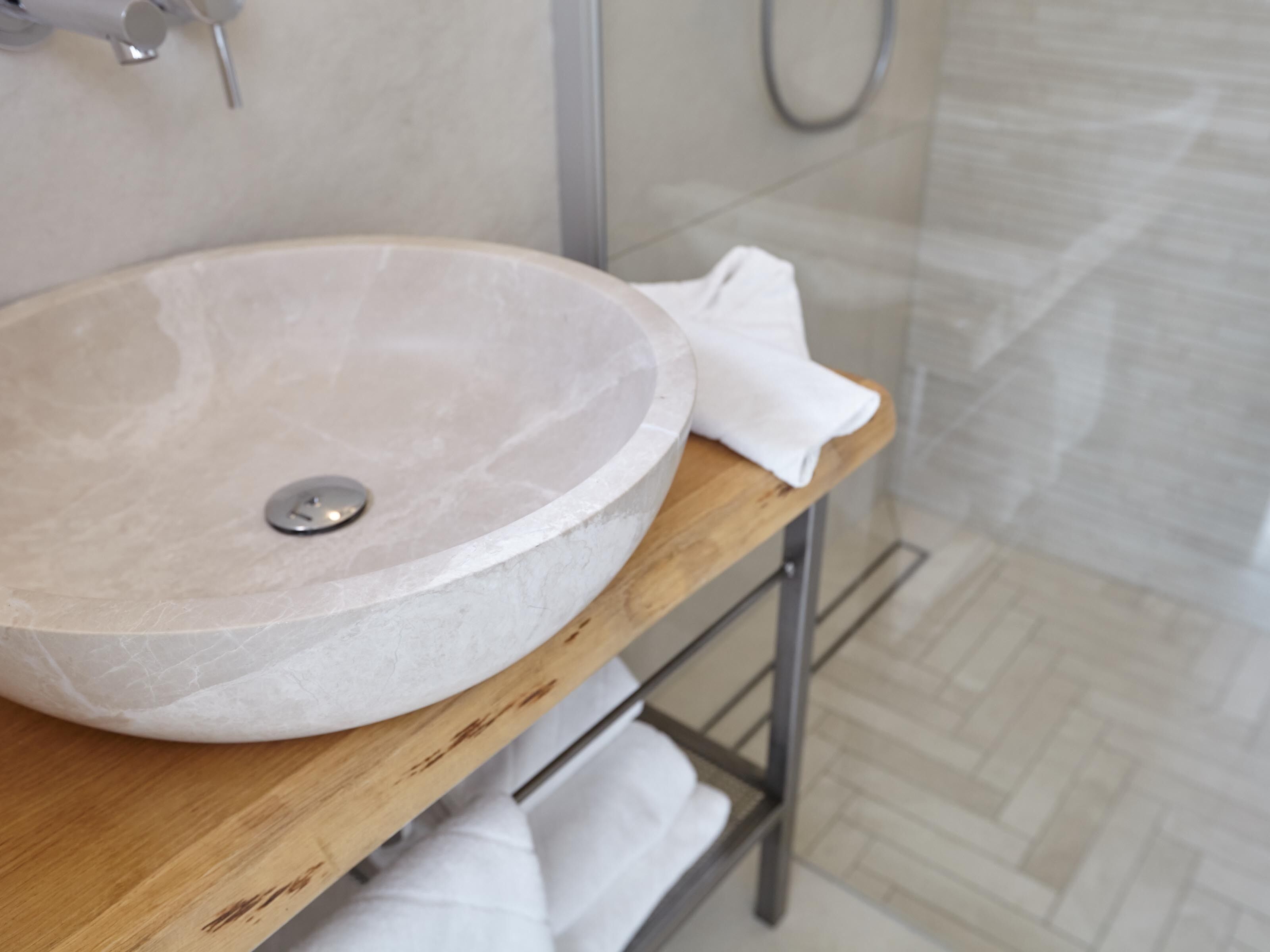 Un lavamanos grande y redondo de mármol sobre una encimera de madera en un baño con piso de baldosas.