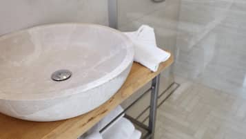 Un lavamanos grande y redondo de mármol sobre una encimera de madera en un baño con piso de baldosas.