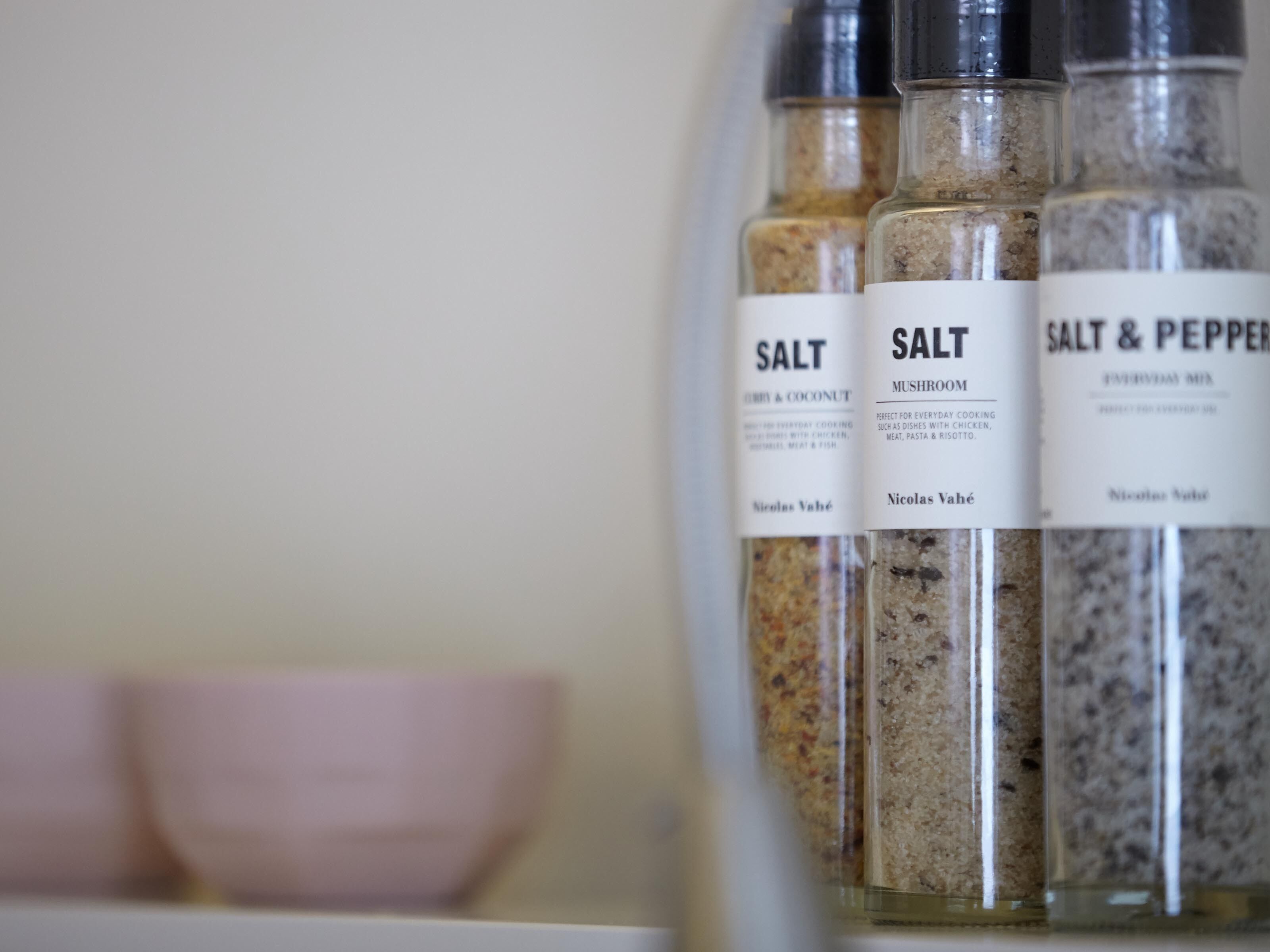 Three glass containers labeled with different types of salt and pepper.