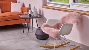 Uma sala de estar moderna com uma cadeira de balanço, um sofá, uma mesa pequena com garrafas e uma janela com vista.