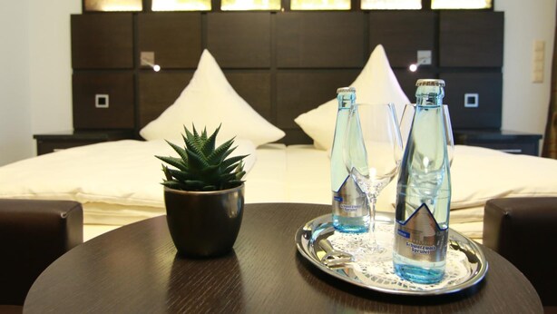 A hotel room with a bed, a bedside table with a potted plant, and two bottles of water on a tray. - Hotel Restaurant Pfeffermühle (Balingen)