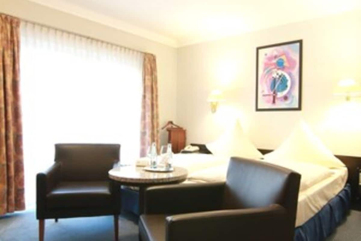 A hotel room with a bed, two armchairs, a small table with a tray, and a painting on the wall.