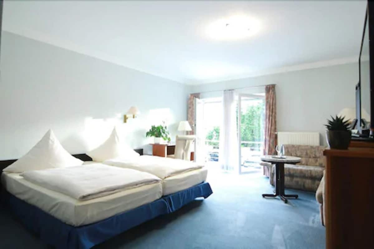 A hotel room with a bed, a small table, a chair, and a view of the outdoors.