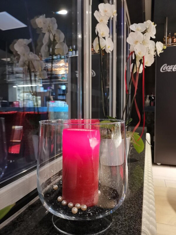 Un florero de vidrio con una vela rosa, orquídeas blancas y perlas sobre una encimera de cocina.