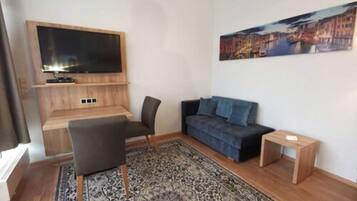Una sala de estar moderna con un televisor de pantalla plana montado en una pared de madera, un sofá azul oscuro, una alfombra estampada y una pequeña mesa auxiliar de madera.