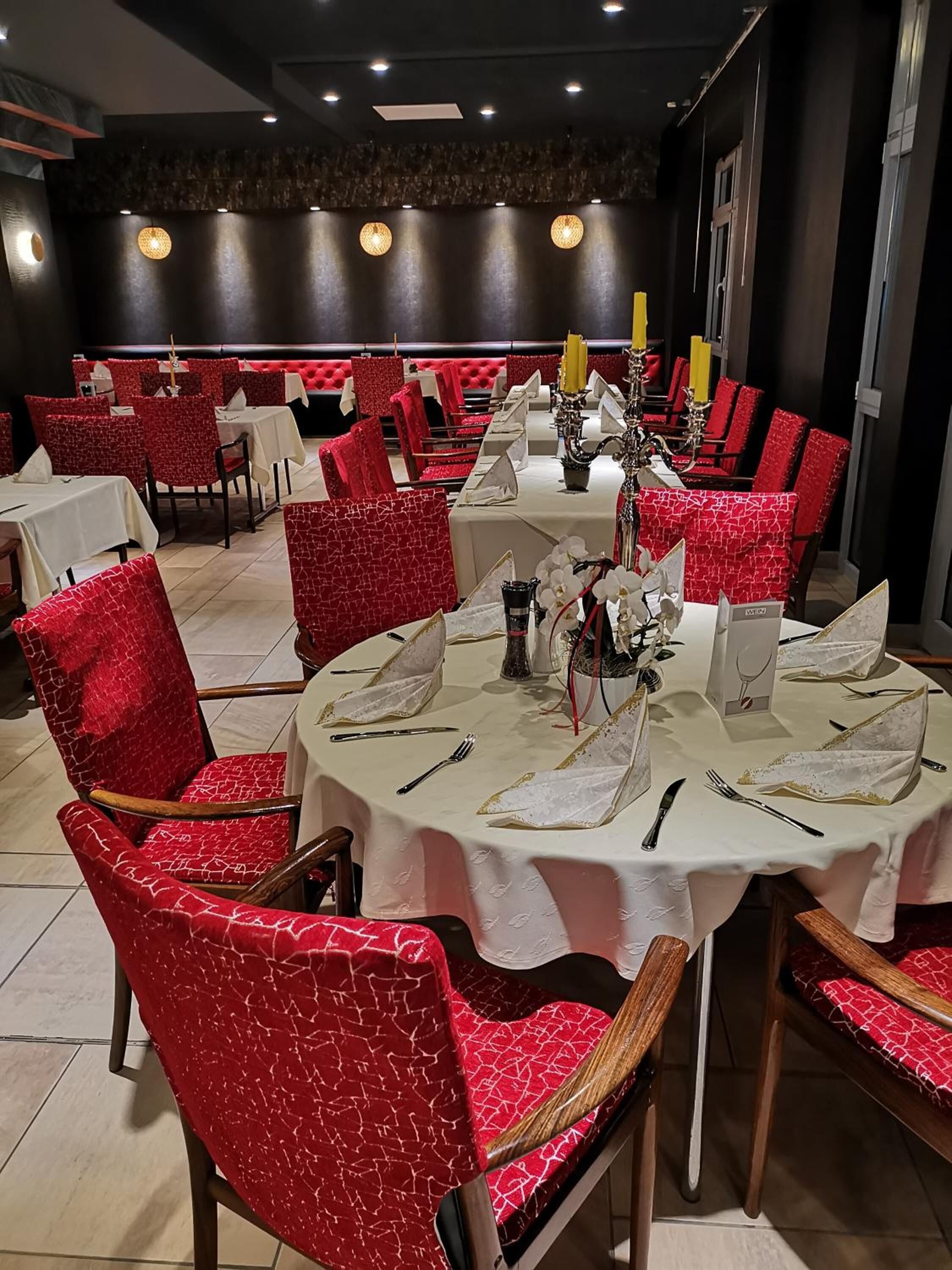 Ein Restaurant mit runden Tischen, roten Sitzmöbeln und weißen Tischdecken.