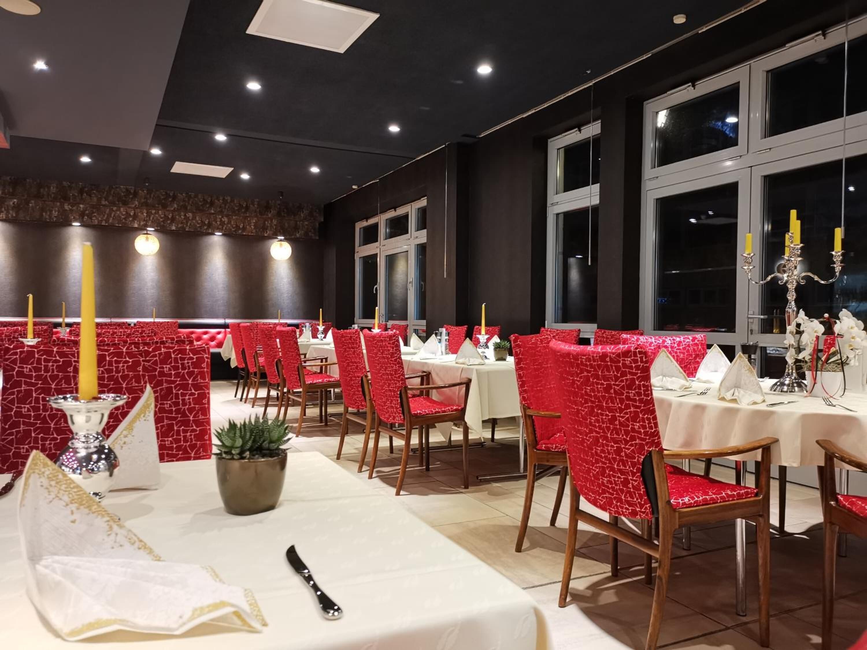 A restaurant with red upholstered chairs, white tablecloths, and candle-lit tables.